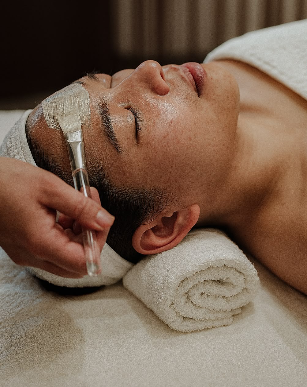 Person receiving a facial treatment with a brush on a towel